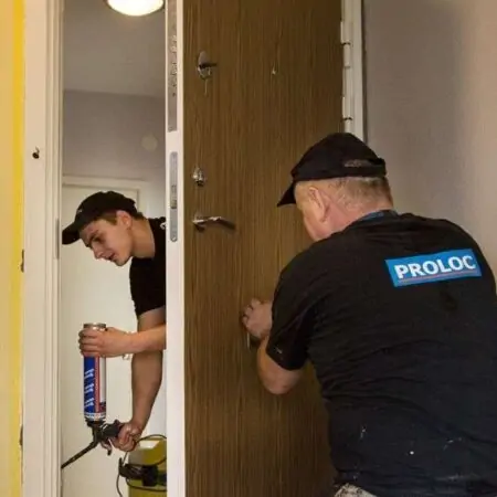 Två hantverkare installerar en säkerhetsdörr med träpanel i Stockholm.