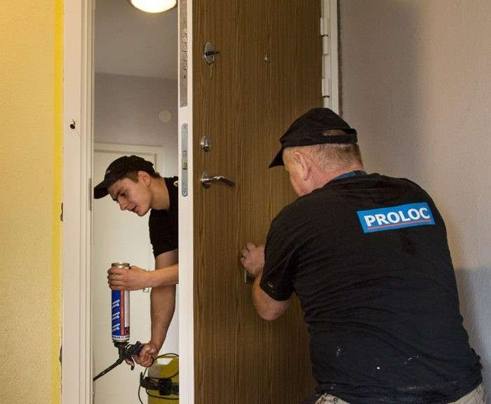 Två hantverkare installerar en säkerhetsdörr med träpanel i Stockholm.